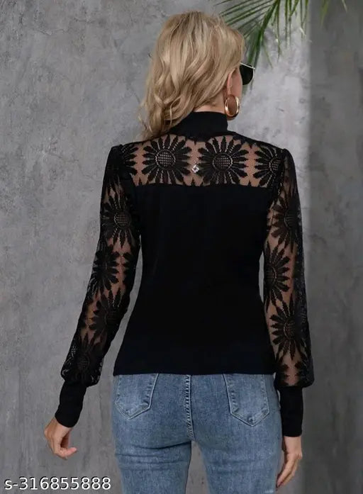 black lace top with floral patterns and blue jeans. She stands against a gray textured wall, exuding a stylish vibe.