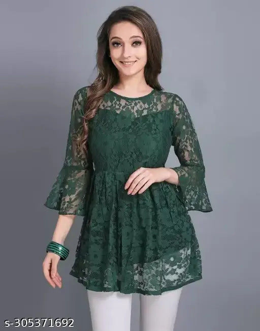 green lace top with flared sleeves, smiling. She pairs it with white pants and green bangles, set against a plain gray background.