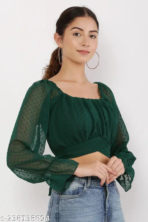  green sheer blouse smiles softly. She wears hoop earrings and jeans, standing against a plain white background. The tone is casual and confident.