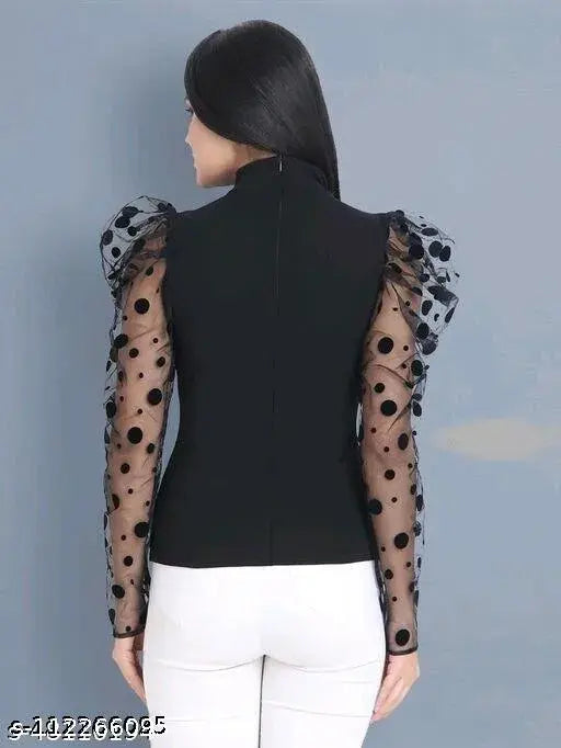 black top with sheer, polka dot long lace sleeves and white pants. Her back is to the camera against a plain gray background.