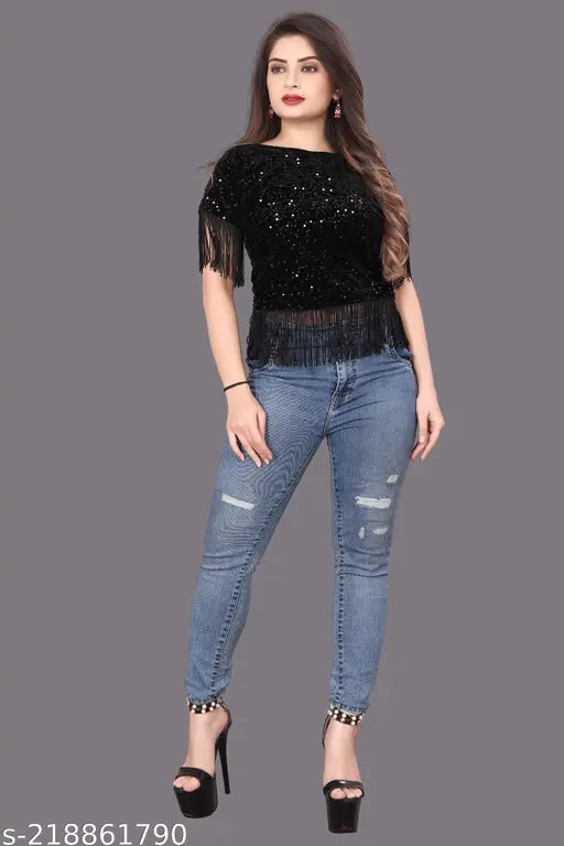 black sequined top with fringe details and jeans wears bright pink earrings.