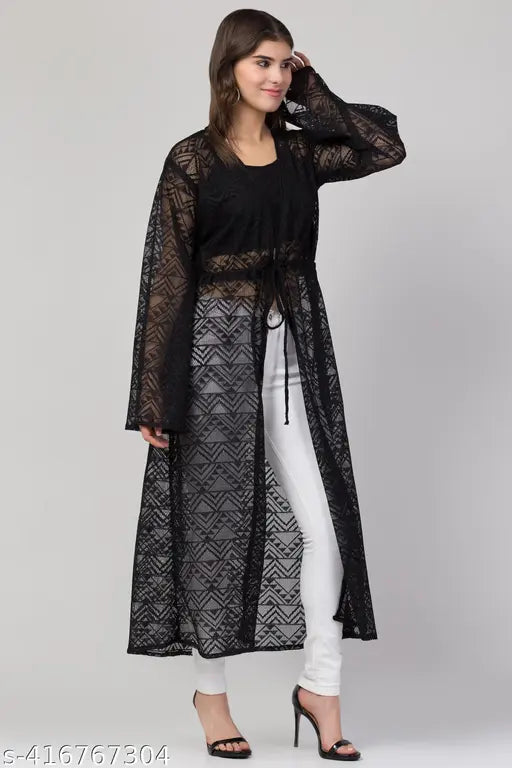 stylish black lace duster over white pants and a black top. She wears black heels, standing confidently against a neutral background.