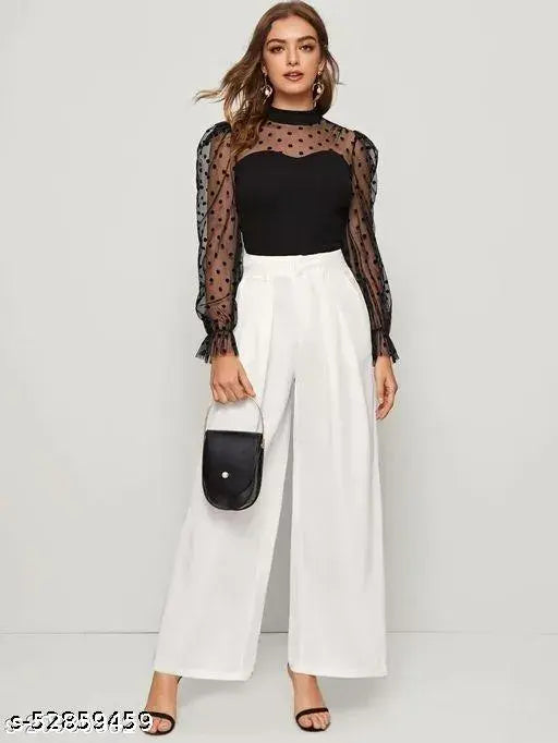 stylish black polka-dot sheer top paired with white wide-leg pants. She carries a small black purse, exuding elegance and confidence.